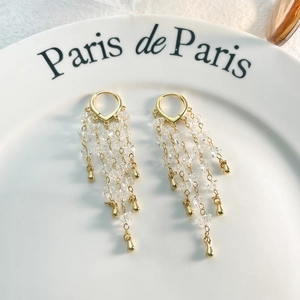 Detailed close-up of 18K gold plated tassel earrings with crystals on a ceramic dish
