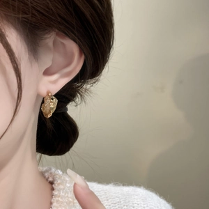 Detailed view of irregular golden textured metal earring on model with elegant curves