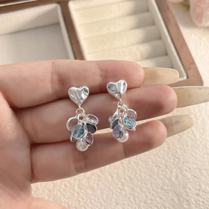 Close-up of heart-shaped silver earrings with colorful zircons and pearls held by hand