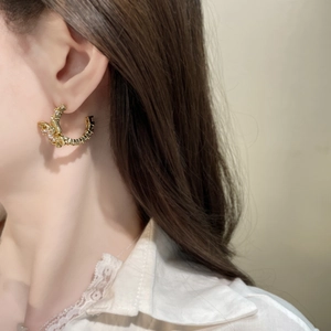 Close-up of golden C-shaped textured earrings worn by a model in warm lighting