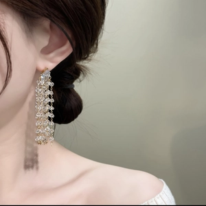 Detail shot of long golden tassel earrings with multi-layered crystal beads on model
