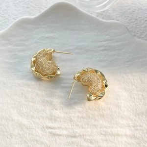 Macro shot of gold irregular wave earrings with woven metal texture and polished finish