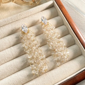 Detailed macro view of gold tassel earrings with rhombic zircons in a beige velvet box
