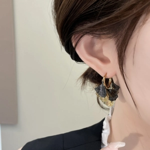 Detail of vintage gold and black ginkgo leaf ear cuffs worn by a model in a suit