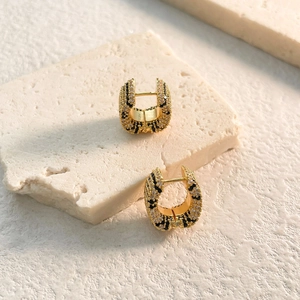Macro shot of gold hoop earrings with zebra pattern micro-inlay on marble stone