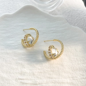 Top view of C-shaped gold earrings with zircon stone on a stone textured tray