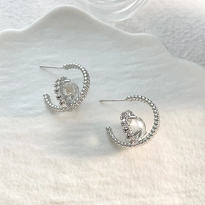 Detailed close-up of 18K silver plated zircon earrings on a white ceramic plate