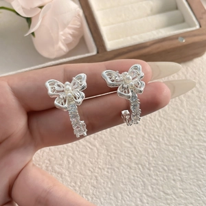 Detail of silver bow earrings with round white pearls and zircon inlay held in hand
