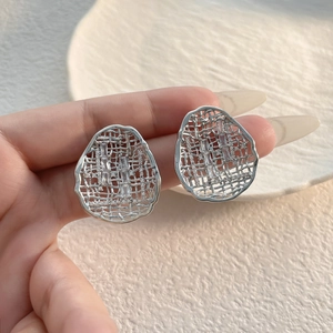 Detailed shot of silver mesh oval earrings with cubic zirconia stones on textured ceramic