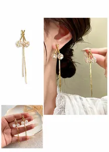 Detalle de elegantes pendientes largos con trébol y borlas en acabados oro y plata