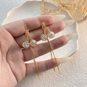 Elegantes pendientes de borla dorados con circonitas mostrados en mano para escala