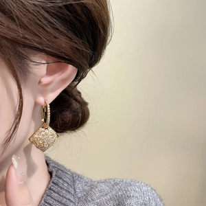 Detailed close-up of diamond-encrusted geometric earrings plated in 18K real gold
