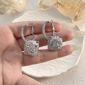 Close-up of silver geometric earrings with pavé zircons and a square charm pendant