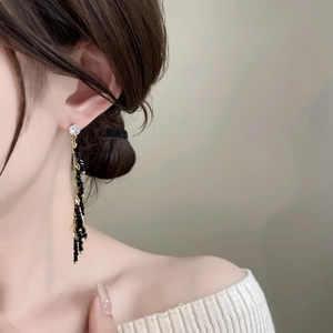 Detail of elegant gold tassel earrings with black beads and zircon on a female model