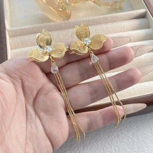 Eleganti orecchini a fiore dorati con nappe e cristalli su una scatola di gioielli