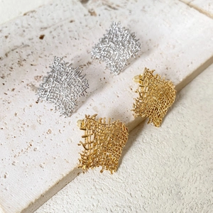 Modern woven metal square earrings in gold and silver finish on stone pedestal