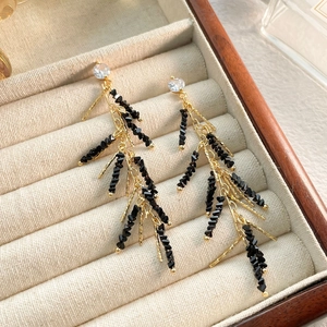 Macro shot of gold tassel earrings with black beads and zircon stones on beige velvet
