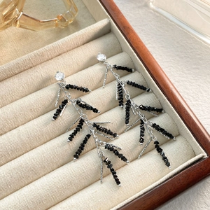 Detailed view of silver tassel earrings with black crystal beads on beige jewelry tray