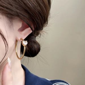 Close-up of gold heart zircon hoop earrings worn by a model in soft lighting