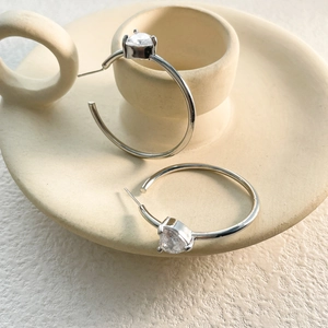 Macro detail of large silver hoop earrings with a pear-cut sparkling zircon drop