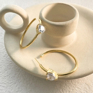 Macro detail of gold hoop earrings featuring heart-shaped cubic zirconia on ceramic base