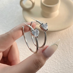Close-up of sparkling heart-shaped zircon silver hoop earrings held by hand