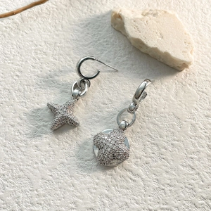 Asymmetric silver star and flower earrings with micro-set zircons on stone background