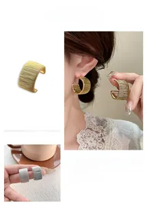 Macro detail of gold and silver woven C-shape earrings with fine industrial brushed texture