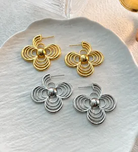 Detail of hollow geometric flower earrings in gold and silver finish on ceramic plate