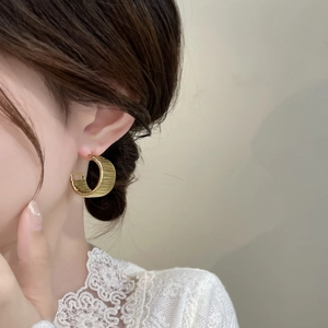 Macro detail of gold C-shaped hoop earrings with woven wire texture on female model