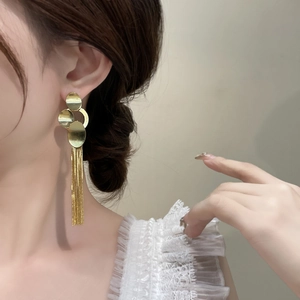 Close-up of elegant gold long tassel earrings with layered discs on a model