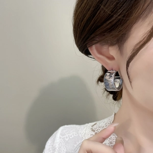Detailed view of silver textured earrings with fine horizontal grooves on a model