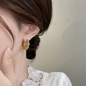 Close-up of golden geometric twisted texture hoop earrings worn on a model's ear