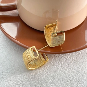 Detail of gold-plated woven texture earrings on a ceramic dish with warm lighting