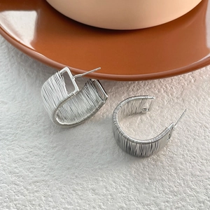 Detail of silver twisted wire wrap C-shape stud earrings on a textured surface