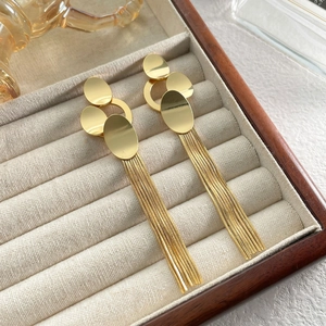 Detailed close-up of gold fringe earrings with polished oval plates and long metal tassels