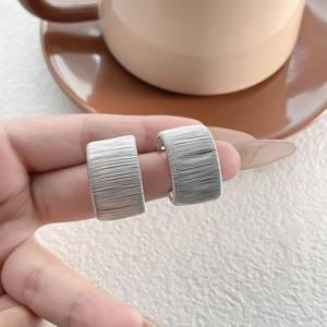 Macro shot of silver-tone stud earrings featuring a textured woven coiled design