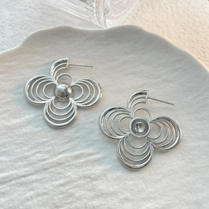 Detail shot of silver four-petal flower earrings with textured concentric line layers