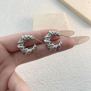 Macro view of silver geometric twisted weave C-shape earrings with a high-shine finish