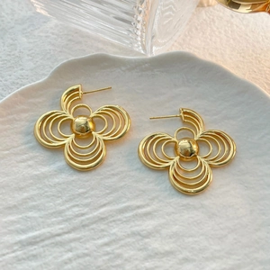 Detailed macro shot of golden tiered flower stud earrings on a textured ceramic dish