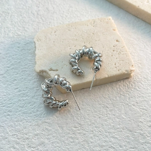 Detail of silver twisted weave hoop earrings on natural stone aesthetic background