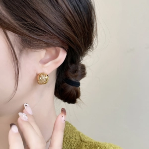 Détail d'une boucle d'oreille dorée en métal tressé avec texture goutte portée par un mannequin