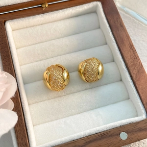 Détail de boucles d'oreilles boules dorées avec texture en maille métallique tressée