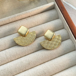 Détail de boucles d'oreilles éventail géométriques aux reflets dorés sur plateau