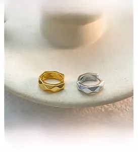 Detail of geometric faceted hoop earrings in gold and silver finish on ceramic tray