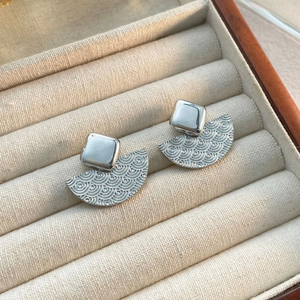 Détail de boucles d'oreilles argentées en forme d'éventail avec motifs de tourbillons texturés