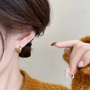Close-up of geometric gold hoop earrings with faceted texture on female model's ear