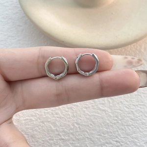 Macro shot of silver geometric hexagonal hoop earrings held on a finger for size reference