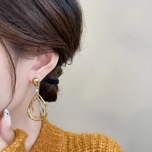 Détail de boucles d'oreilles dorées irrégulières avec zircon brillant portées par un mannequin