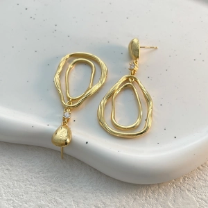 Détail de boucles d'oreilles doubles boucles dorées irrégulières avec zircon sur plateau